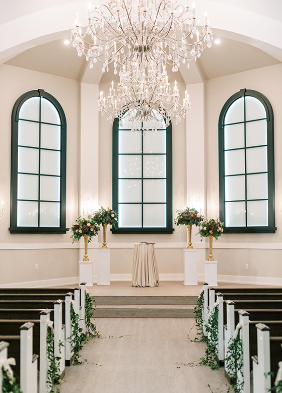 View down the aisle in the white chapel with black and wood accents and chandelier