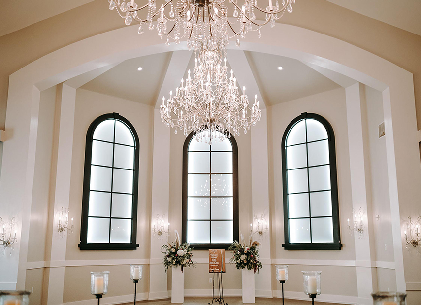 View down the aisle in the white chapel with black and wood accents and chandelier