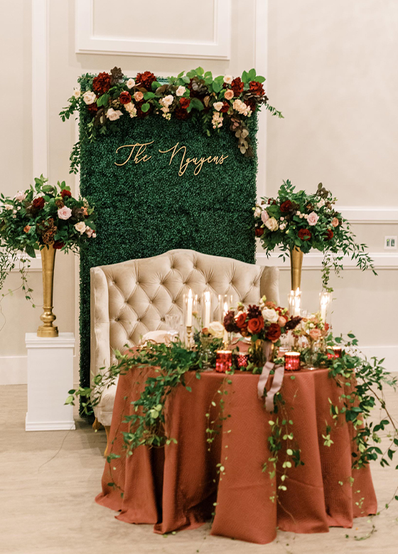 Decadent sweetheart table with custom florals, monogram, and greenery on table with rust cloth