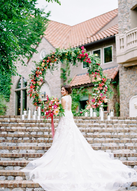 Bride walking up brick and stone stairs towards floral circle with red and pink roses
