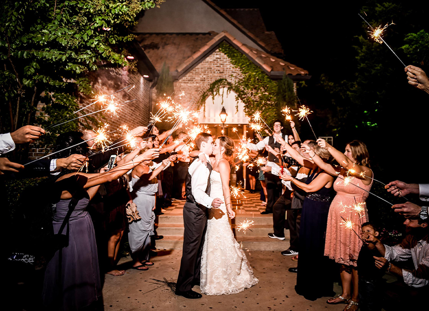 Bride and groom kissing at night in front of venue entrance with sparkler send-of