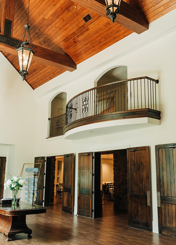 View looking up at balcony with red wood ceiling and modern chandelier