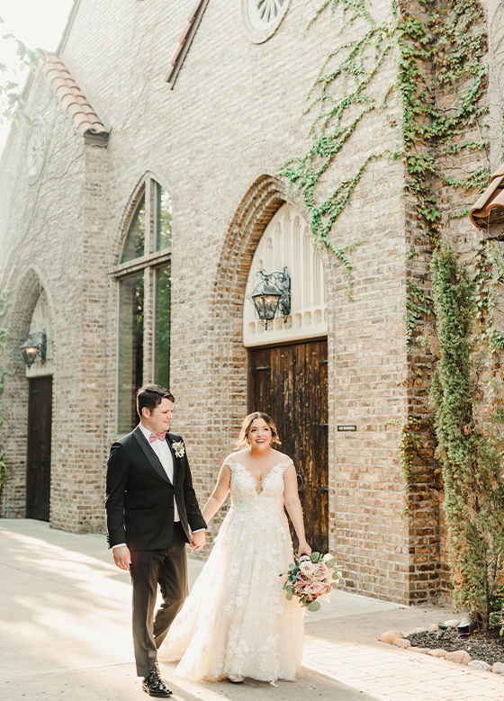 Bride and groom holding hands walking outside Tuscan-style light brick entrance