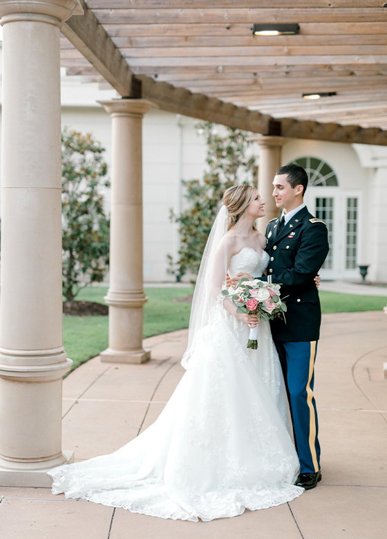 Bride and groom in military uniform standing outdoors under stone columns