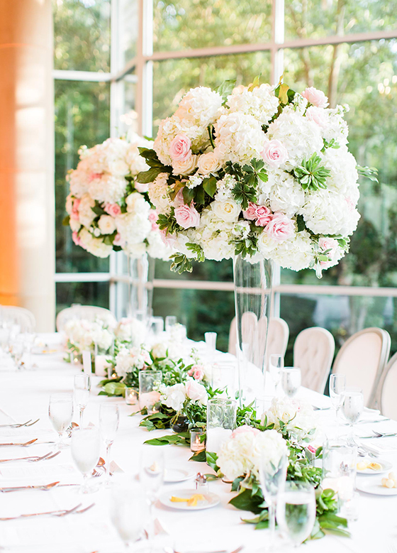 Long table in front of floor to ceiling windows with pillar centerpieces of pink and white roses