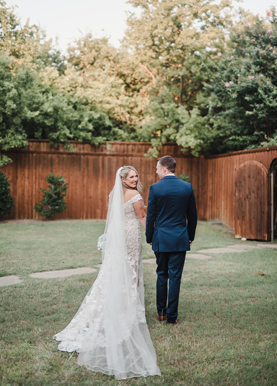 Bride looking over her shoulder at camera in outdoor space with trees and wood fence