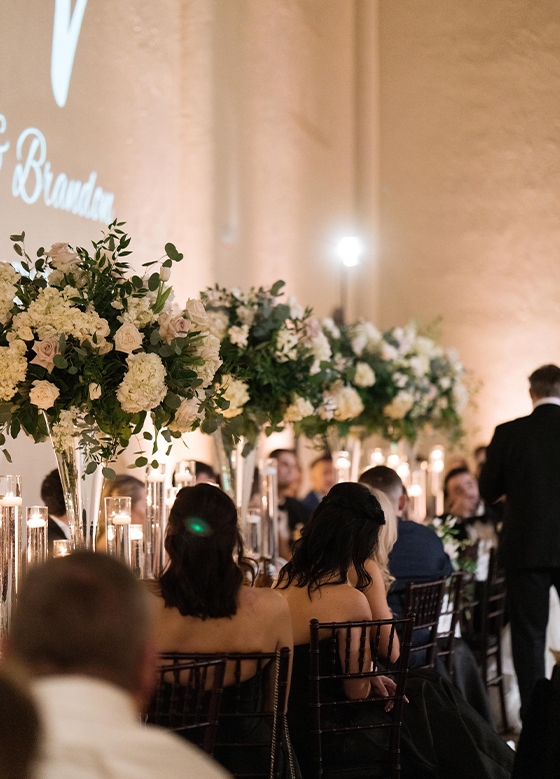 Long table with pillar centerpieces of white roses with guests seated facing away