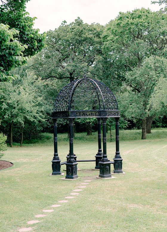 Black wrought iron gazebo outside with lush forest in background