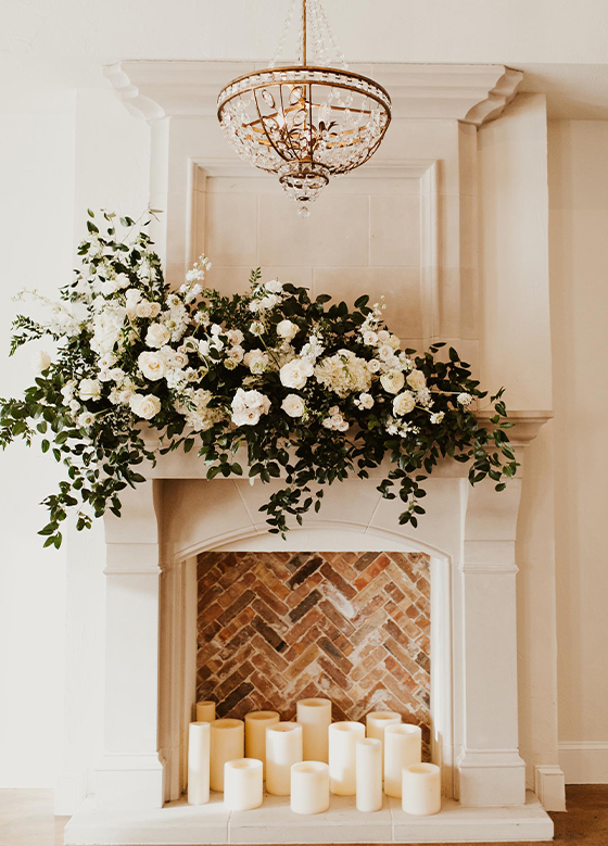 View of white modern fireplace with white florals on mantle and pillar candles inside