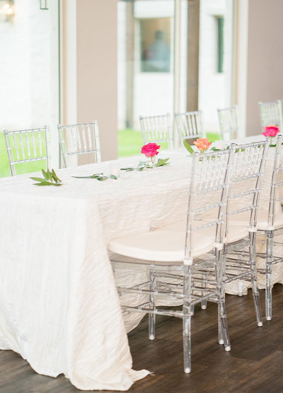 Banquet table with clear chairs looking out on grounds via floor to ceiling windows