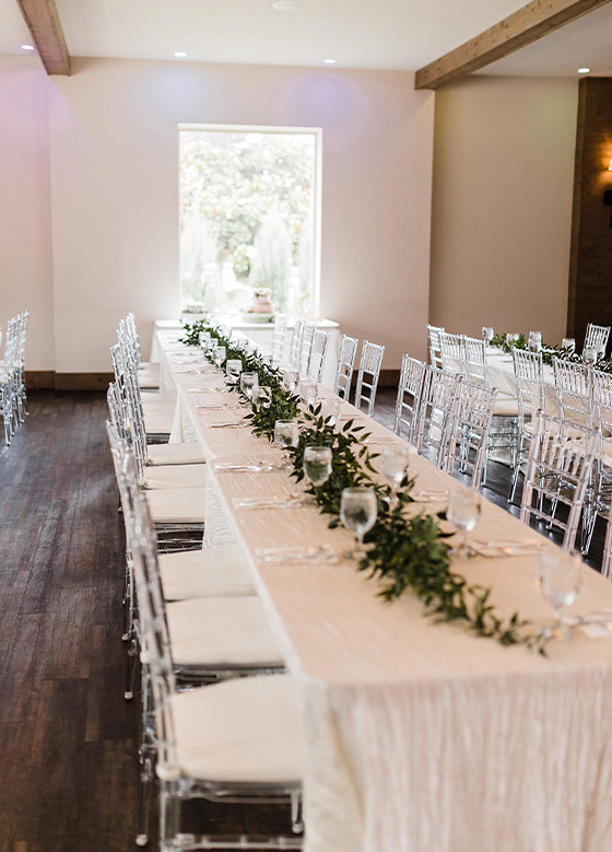 View looking down banquet table with clear chairs and greenery runner