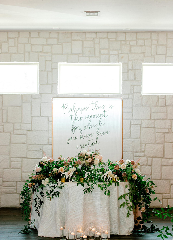 View of sweetheart table with greenery, florals, and custom sign behind
