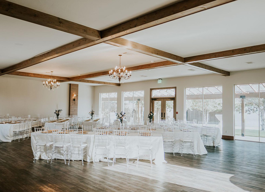Reception set up with banquet tables whit ceilings with dark wood beams and chandeliers