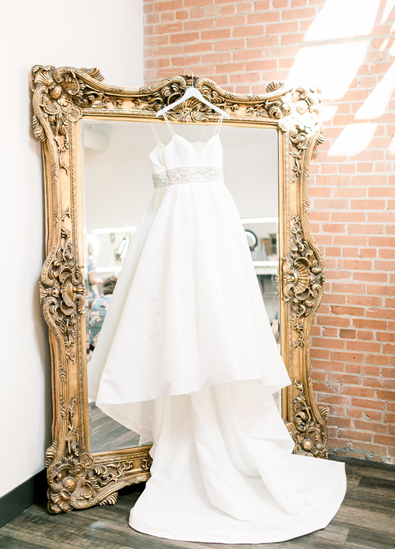 Close up of bridal gown hanging on gold mirror next to brick wall