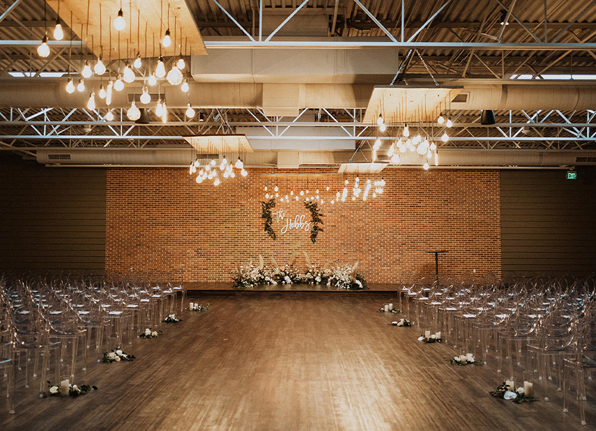 View up aisle of custom monogram on brick wall with clear chairs
