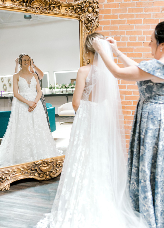 Bride standing in front of gold mirror while her mother puts her veil on