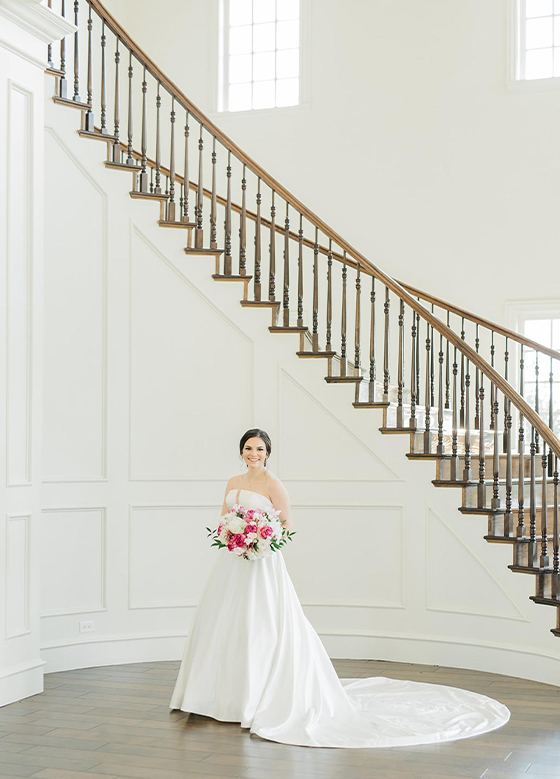 Bride standing next to grand white staircase with wood accents