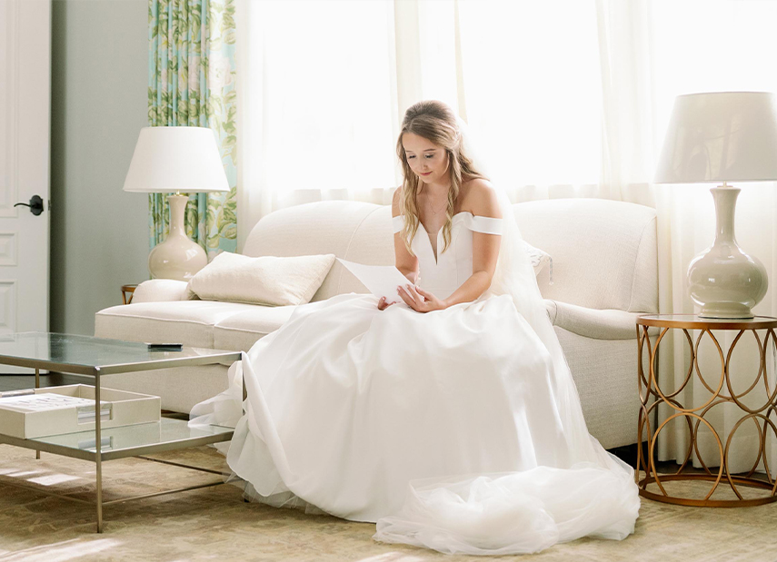 Bride in Bridal Suite Reading Letter on White Couch