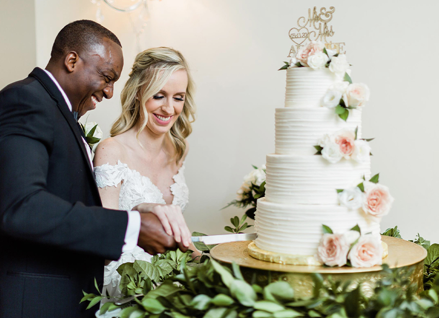 Bride and groom cutting a white tiered wedding cake decorated with flowers