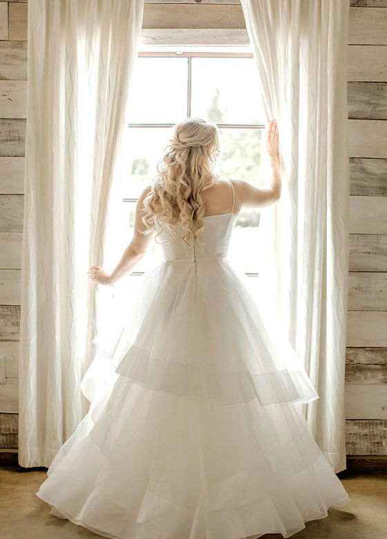 Bride in white dress looking out window
