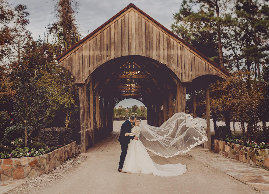 Bride and groom kissing in front of covered bridge