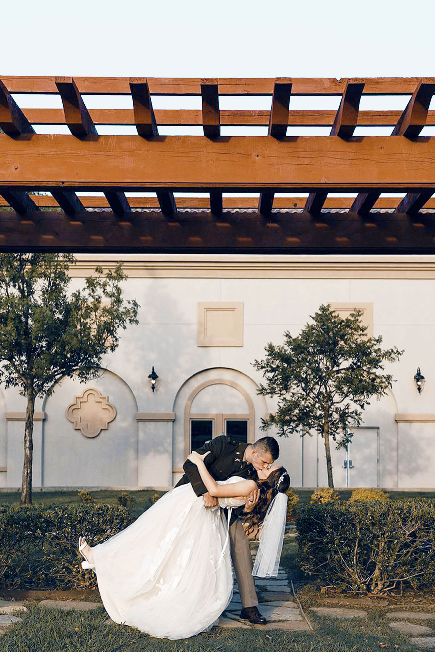 Groom dipping and kissing bride in front of modern venue