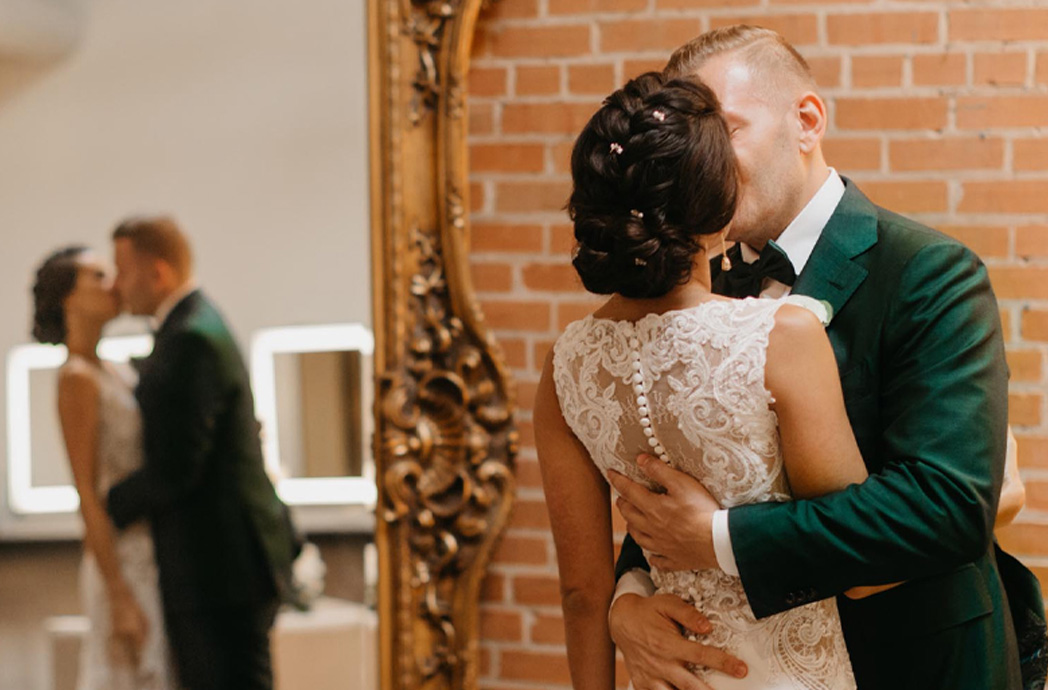 Bride and groom kissing in front of brick wall and gold mirror